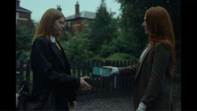 One woman giving a younger woman a smartphone, with houses and trees in the background.